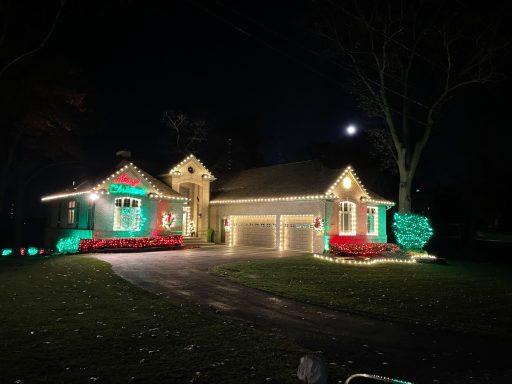 A house decorated with colorful lights and festive landscaping at night.