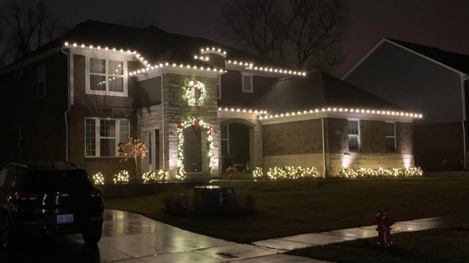 A decorated house with white lights and a wreath, set in a nighttime scene.