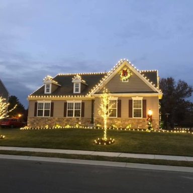 A house decorated with festive lights and a small illuminated tree in the yard.