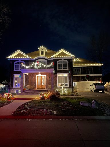 A decorated house at night with festive lights and a holiday wreath on the door.